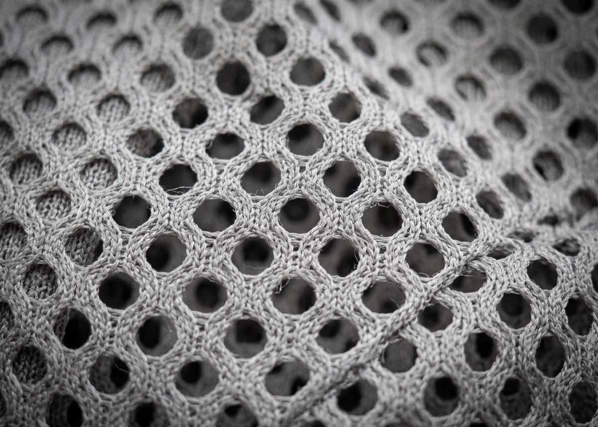 Close macro shot of mesh polyester fabric, open perforated weave with visible negative space.