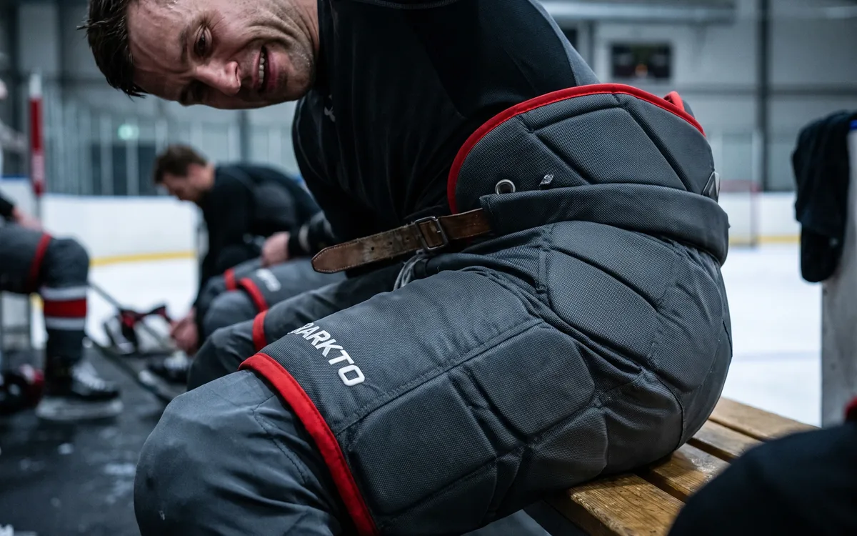Athlete in graphite pro-level hockey pants showing inner-thigh reinforcement and segmented padding lines