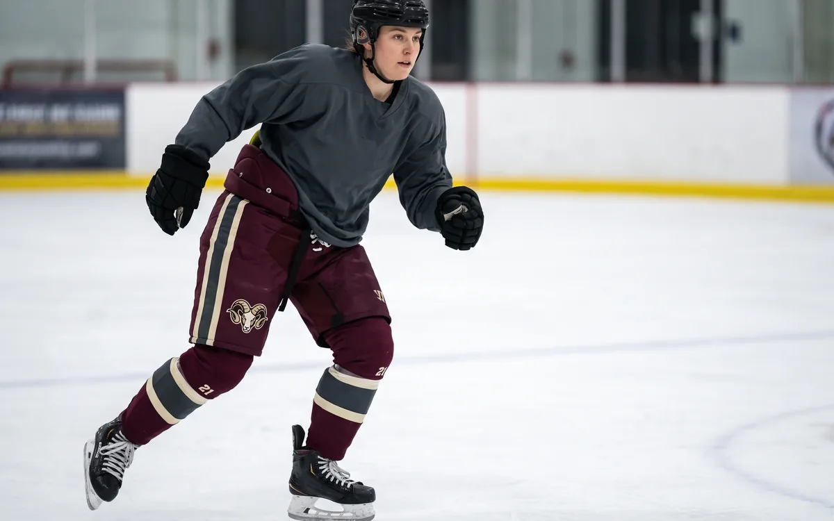 Female player mid-stride in burgundy women's-fit hockey pants with a ram crest and number 21