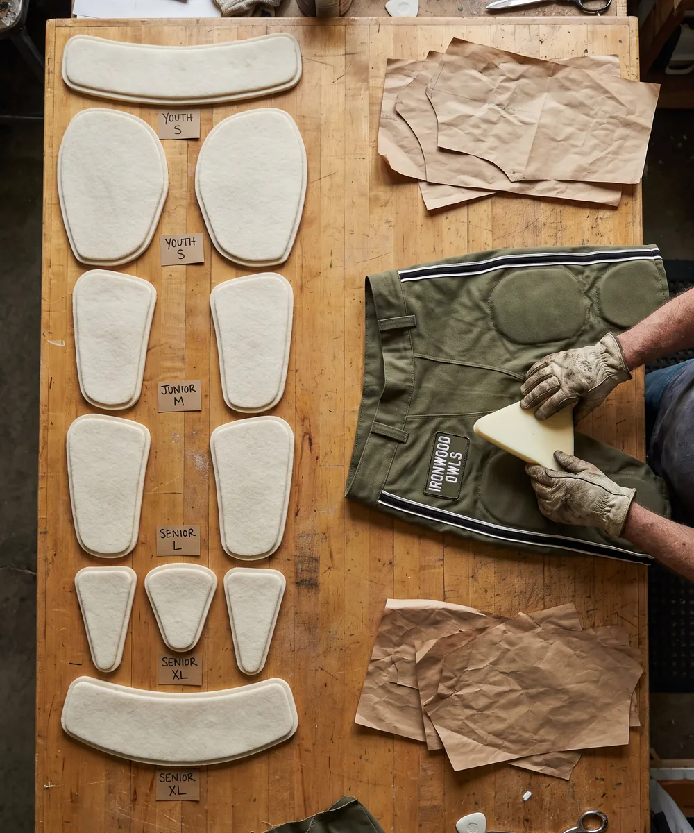 Hip, outer thigh, tailbone, lower back and inner-thigh padding pieces laid out by size from youth small to senior extra large beside an olive pant shell