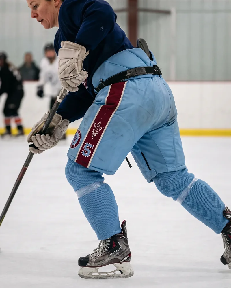 Female player in a long stride wearing powder blue anatomical-fit hockey pants with a maroon stripe