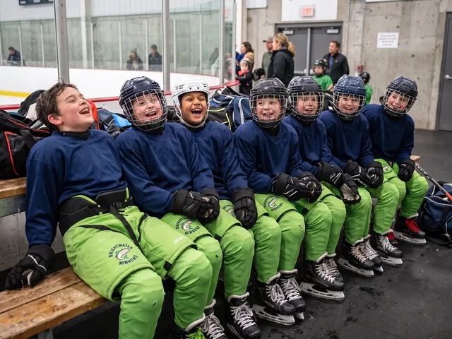 Youth players laughing on the bench in lime green and black hockey pants