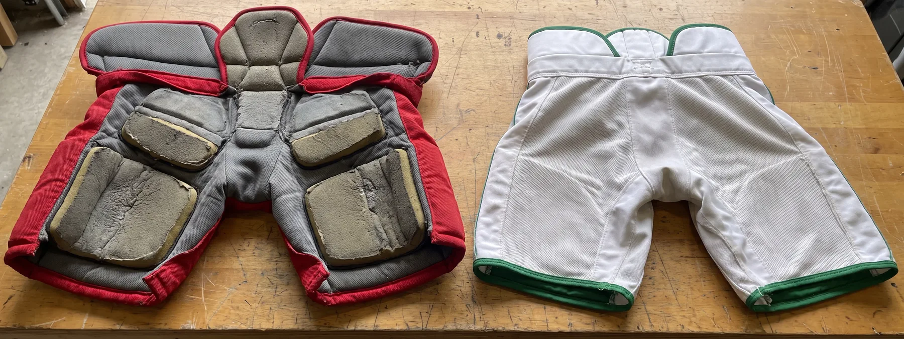A complete padded hockey pant lying open beside an unpadded hockey pant shell to show the difference inside