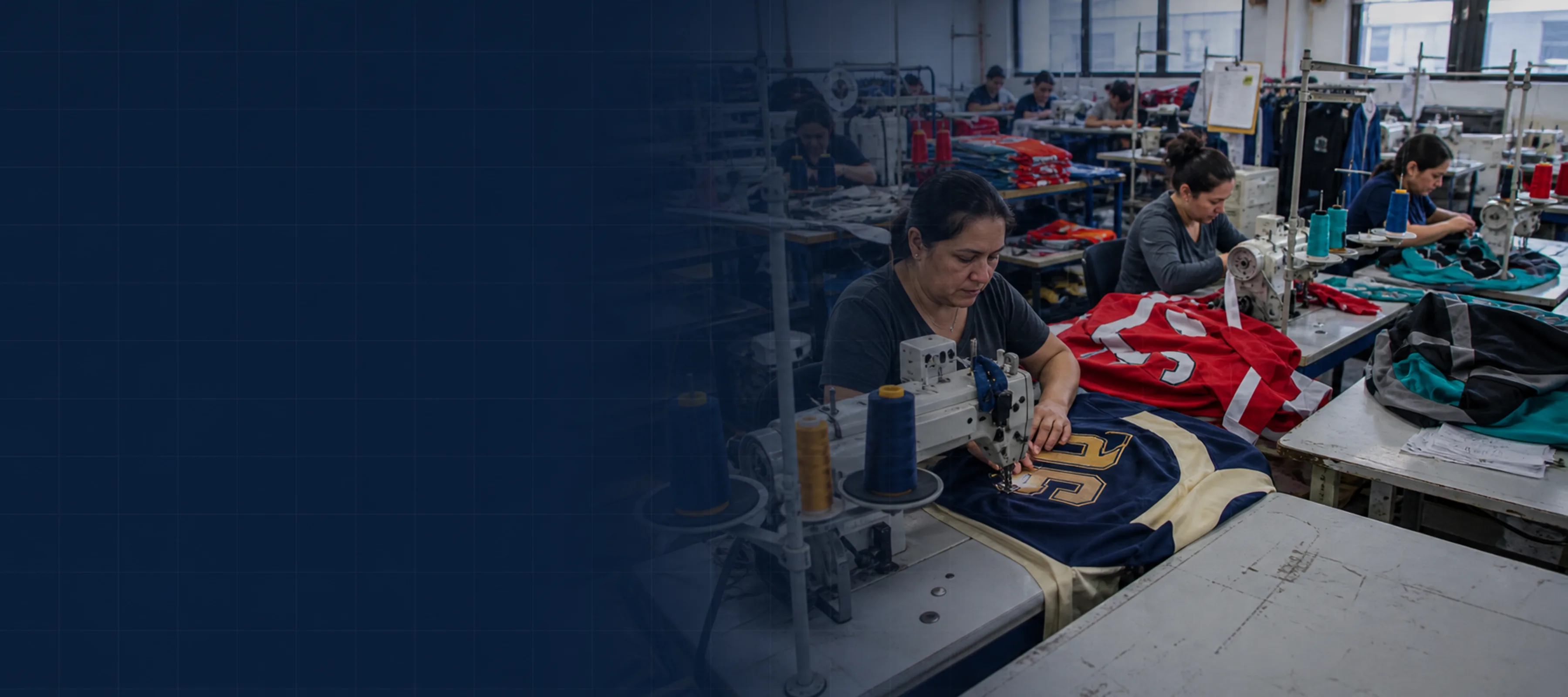 Wide-angle factory floor with several sewing stations, at least three different garment colorways visible in progress