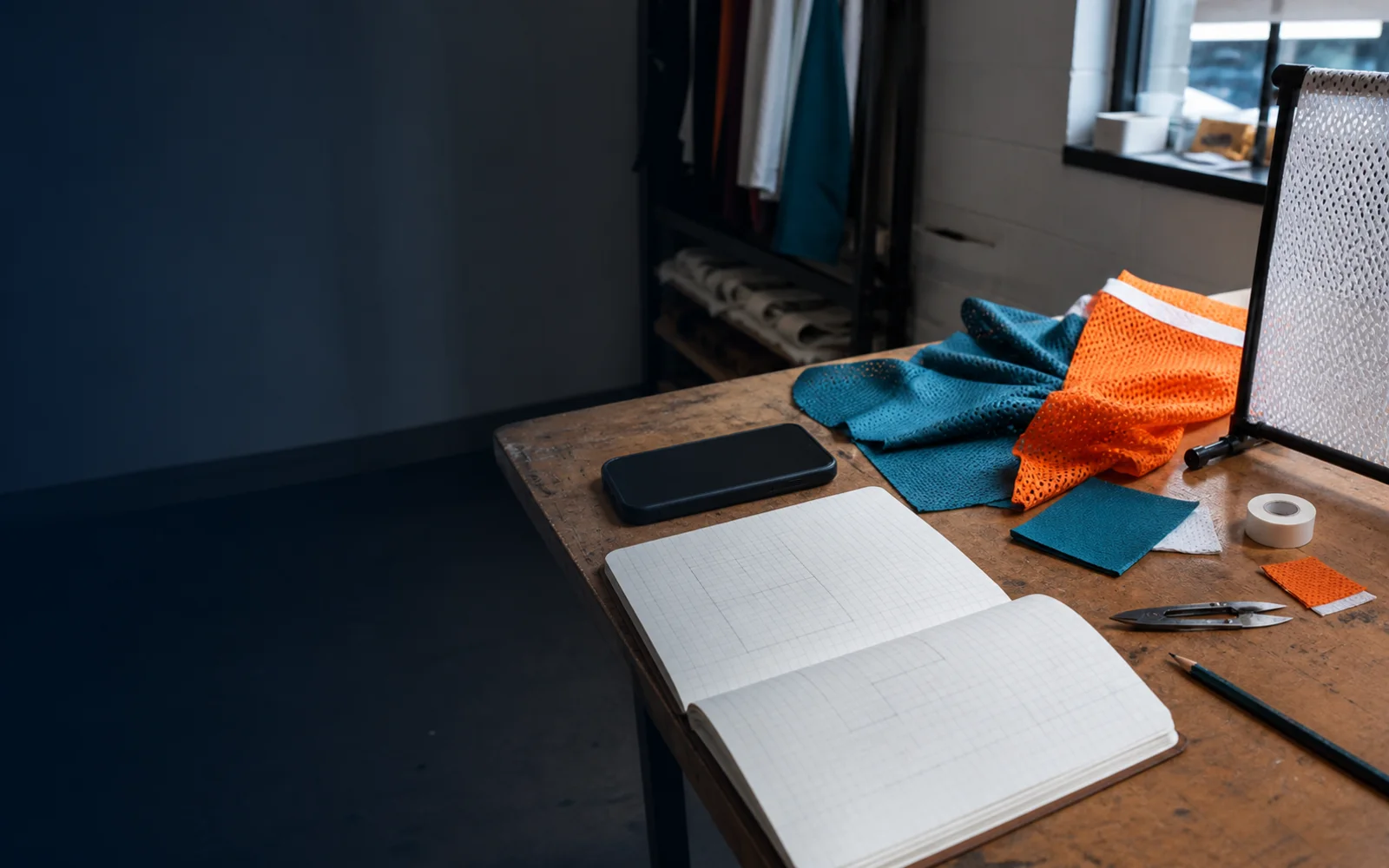 A quiet inquiry-side workspace: a notebook, fabric swatches, and a phone face down on a plain desk
