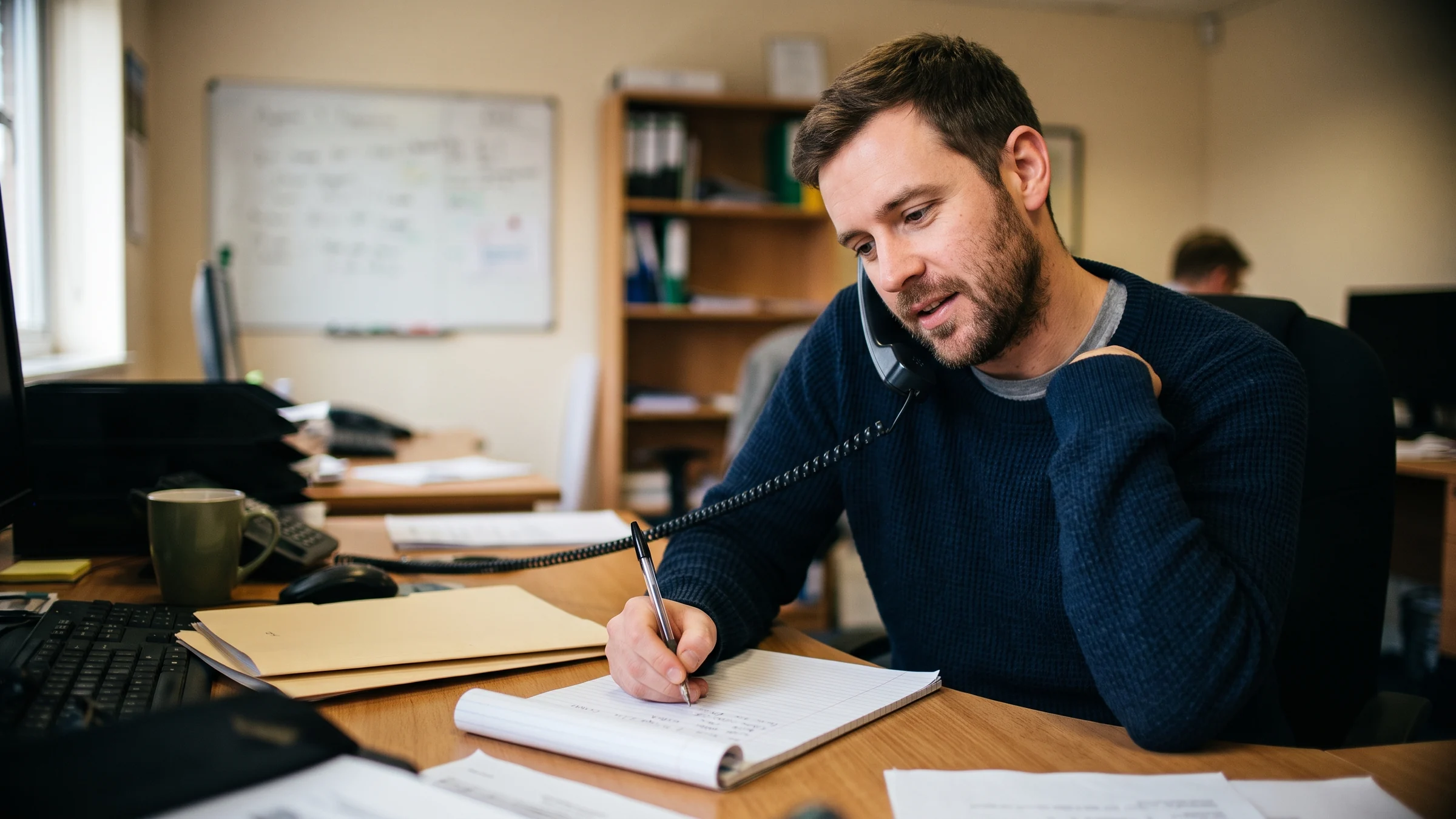 A staff member on a call taking notes on a fresh account setup sheet at a desk.